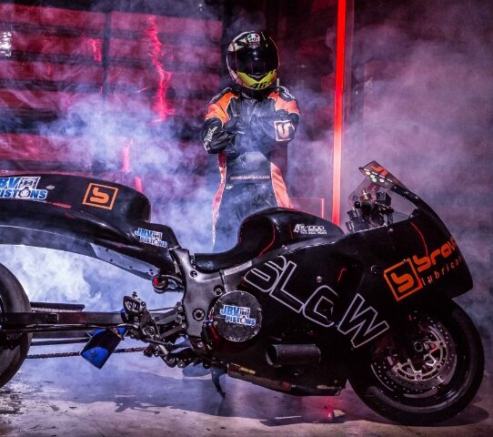 man wearing helmet standing next to a brava branded motorcycle in a smokey atmosphere